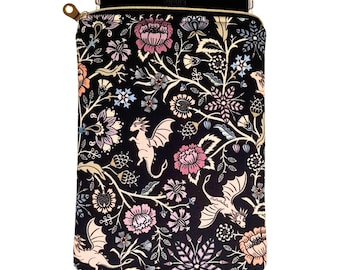May include: A black fabric sleeve for an e-reader featuring a repeating pattern of light pink dragons, various flowers, and leafy vines in shades of pink, blue, and cream. The sleeve has a gold-toned metal zipper closure at the top edge.