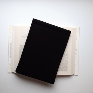 May include: A black book cover rests on an open book with text visible. The book's pages are off-white, and the cover is a solid, matte black. The text on the book is partially visible, with the words "Nurturing Sleep, Dreams" at the top.