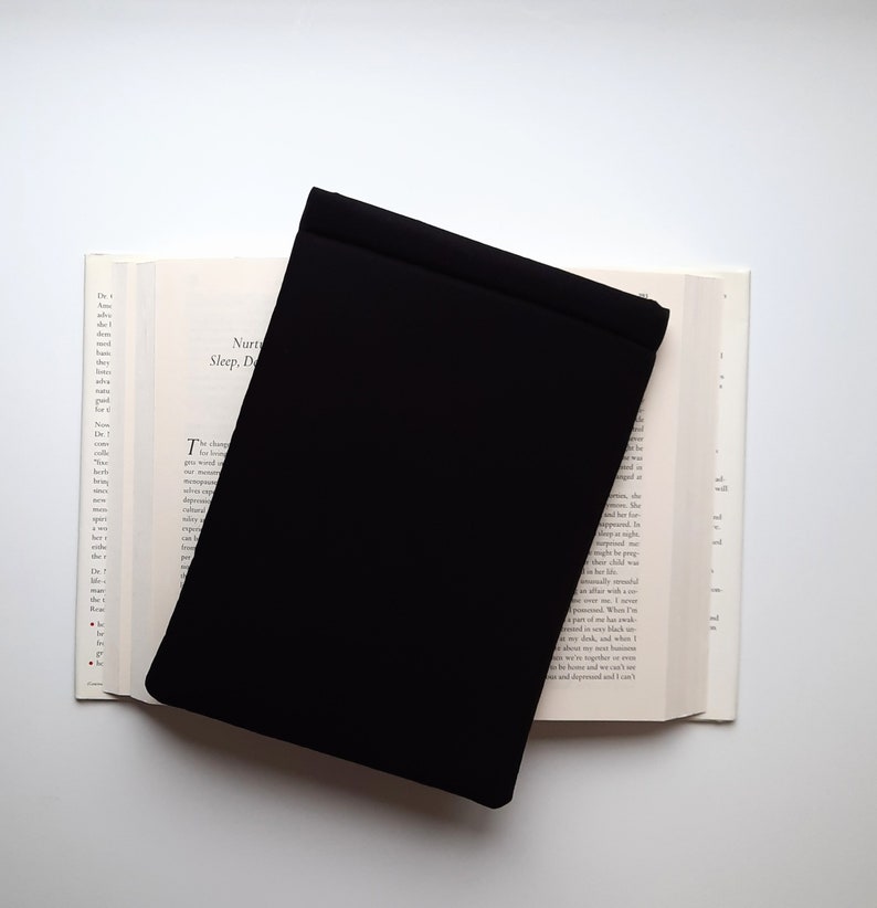 May include: A black book cover rests on an open book with text visible. The book's pages are off-white, and the cover is a solid, matte black. The text on the book is partially visible, with the words "Nurturing Sleep, Dreams" at the top.