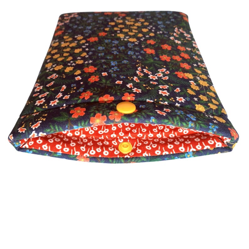 May include: A floral print case with a navy blue exterior and a red interior. The navy blue fabric features small orange, yellow, and blue flowers. The interior is red with a white floral pattern. It fastens with two yellow snap closures.