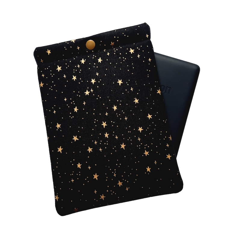 Puede incluir: Una funda negra de tela para lector electr&oacute;nico con estrellas doradas. La funda est&aacute; doblada sobre un lector electr&oacute;nico negro.