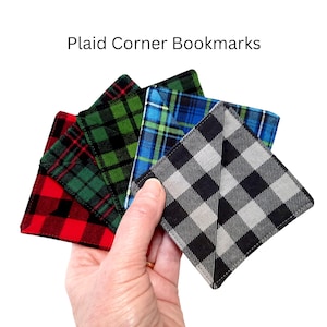 May include: Plaid corner bookmarks in red, green, blue, and black and gray. The bookmarks are held in a hand and have a corner pocket design. The text "Plaid Corner Bookmarks" is at the top of the image.