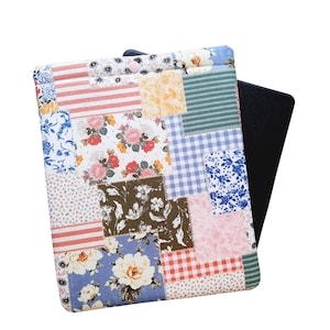 May include: A patchwork tablet sleeve featuring a variety of floral, striped, and gingham patterns in shades of pink, blue, yellow, and brown. The sleeve has a button closure and a black tablet peeking out from the side.