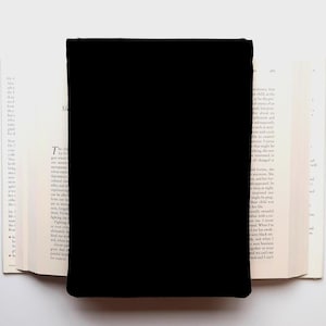 May include: A black rectangular object covers the center of an open book. The book's pages are off-white, with printed text visible on the left page. The background is a plain white surface.