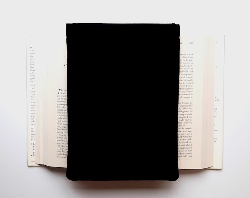 May include: A black rectangular object covers the center of an open book. The book's pages are off-white, with printed text visible on the left page. The background is a plain white surface.