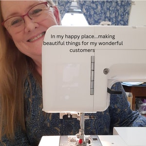 May include: A white sewing machine with the text "In my happy place...making beautiful things for my wonderful customers." The machine is in use, with the needle and presser foot visible. The background includes a person wearing glasses.