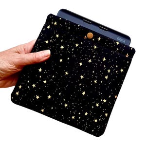 May include: Black and gold star-patterned tablet sleeve with a snap closure. The sleeve holds a black tablet with the brand name "Kobo" visible. The sleeve is held in a hand.