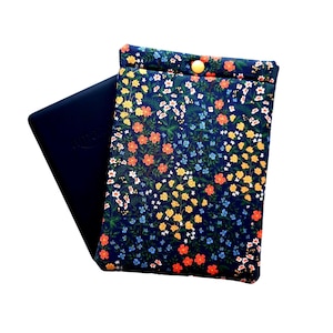 May include: A navy blue floral print case with a yellow button closure. The case is open, revealing a dark blue electronic device. The floral pattern includes orange, yellow, white, and blue flowers on a dark blue background. The case is designed to protect the device.