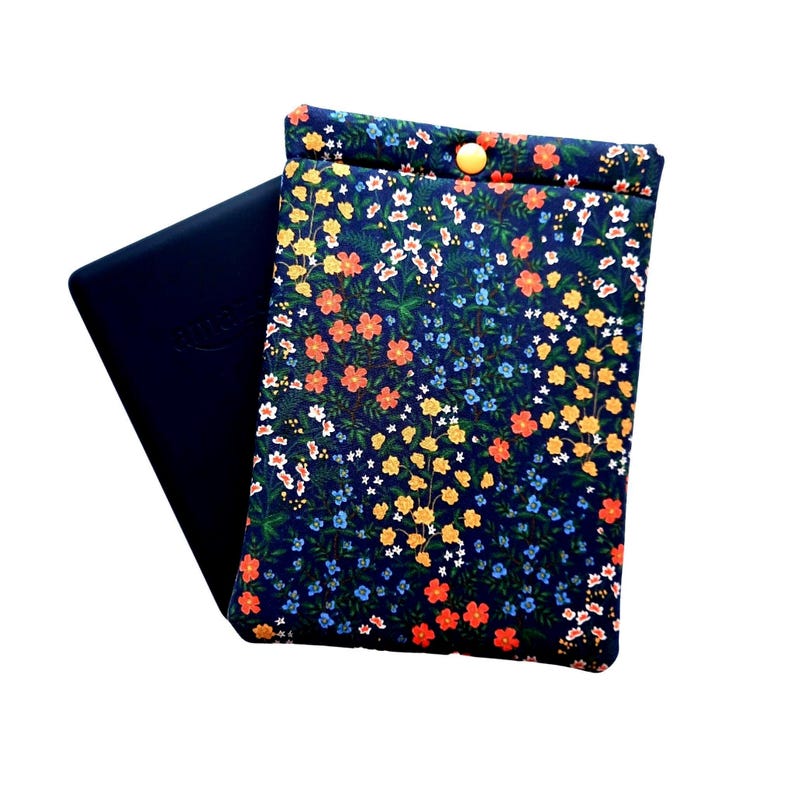 May include: A navy blue floral print case with a yellow button closure. The case is open, revealing a dark blue electronic device. The floral pattern includes orange, yellow, white, and blue flowers on a dark blue background. The case is designed to protect the device.