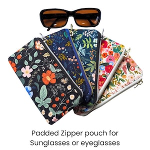 May include: Black sunglasses rest above five floral-patterned padded zipper pouches. The pouches feature various floral designs in colors like red, orange, blue, and white. The text at the bottom reads "Padded Zipper pouch for Sunglasses or eyeglasses."