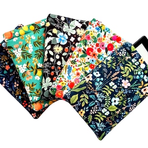 May include: A collection of colorful fabric e-reader sleeves with floral patterns. The patterns include a teal design with lemons, a black design with white flowers, and a navy design with small white flowers. An e-reader is partially visible.