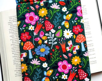 May include: A dark green book sleeve featuring a colorful floral pattern. The design includes pink, red, yellow, and blue flowers, along with butterflies and mushrooms. The sleeve is open, holding a book.