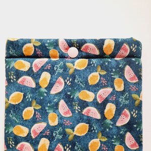 May include: A teal fabric case with a repeating pattern of yellow lemons and pink watermelon slices. The design includes green leaves and small pink floral accents. A light pink button secures the flap.