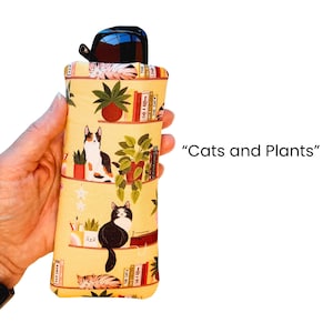 Pu&ograve; includere: Un astuccio giallo per occhiali con un motivo ripetuto di gatti, piante e librerie. L'astuccio contiene un paio di occhiali da sole. Il testo "Cats and Plants" &egrave; stampato sul lato destro.