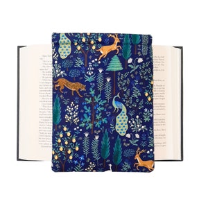 May include: A navy blue book cover with a whimsical forest design. The cover features illustrations of a leopard, deer, and peacock amidst trees and foliage. The cover is open, revealing the pages of a book.