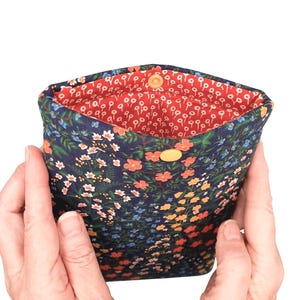 May include: A small pouch with a floral pattern. The exterior is navy blue with a design of colourful flowers. The interior is bright red with a white floral design. It has a yellow button closure.