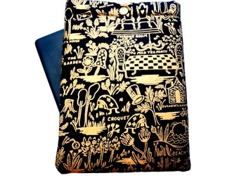 May include: Black and gold fabric book cover featuring a whimsical illustration of a tea party scene from Alice in Wonderland. The illustration includes text such as "The Garden", "Mad Tea Party", "Throne Room", and "Croquet".
