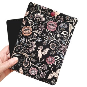 May include: Black fabric e-reader case with a floral and dragon print. The case has a red button closure.