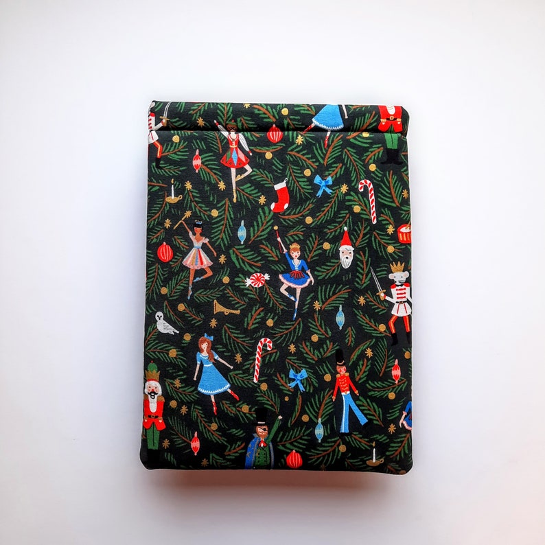 May include: A rectangular fabric pouch featuring a black background with a repeating pattern of green pine branches, red and blue ornaments, candy canes, and figures including nutcrackers, ballerinas, and a bearded man in a red hat.