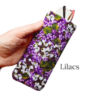 Pu&ograve; includere: Un astuccio per occhiali in tessuto con un motivo floreale di fiori viola e bianchi e foglie verdi. L'astuccio contiene un paio di occhiali. La parola "Lilacs" &egrave; stampata sull'astuccio.