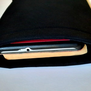 May include: Black fabric sleeve, possibly for a tablet or e-reader, with a device partially visible inside. The device has a black frame, a red border, and a light-colored backing.