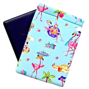 May include: A blue e-reader case with a fun flamingo print. The light blue case features pink flamingos, palm trees, and beach scenes. A dark blue e-reader is partially visible inside the case.
