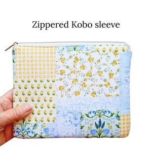 May include: A patchwork zippered Kobo sleeve with a variety of floral and gingham patterns in yellow, blue, and white. The sleeve has a gold zipper and is held by a hand. The text "Zippered Kobo sleeve" is at the top.