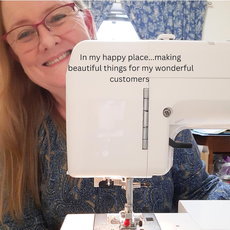 Pu&ograve; includere: Una macchina da cucire bianca con la scritta "In my happy place...making beautiful things for my wonderful customers". La macchina ha un ago argentato e una bobina di filo rossa. La macchina &egrave; su una superficie bianca.