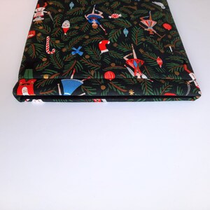 May include: A rectangular fabric sleeve featuring a black background with a repeating Christmas-themed pattern. The print includes green pine branches, red stockings, candy canes, ornaments, and figures of nutcrackers and dancers in colorful outfits.