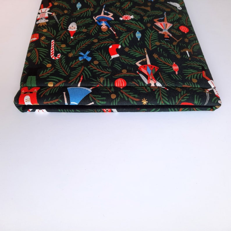 May include: A rectangular fabric sleeve featuring a black background with a repeating Christmas-themed pattern. The print includes green pine branches, red stockings, candy canes, ornaments, and figures of nutcrackers and dancers in colorful outfits.