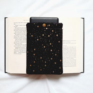 Puede incluir: Funda para lector electr&oacute;nico de terciopelo negro con un patr&oacute;n de estrellas doradas. La funda tiene un cierre de bot&oacute;n.