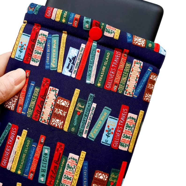 May include: A navy blue fabric book sleeve with a pattern of colorful book spines. The sleeve has a red button closure and is designed to hold a tablet or e-reader.