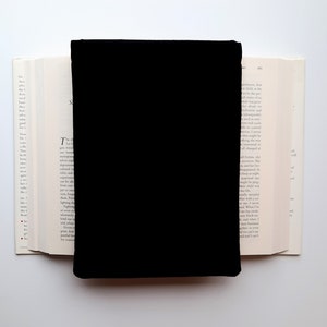 May include: A black book cover is centered on an open book with white pages. The book's pages are visible on either side of the black cover, creating a contrast between the dark cover and the light pages. The background is white.