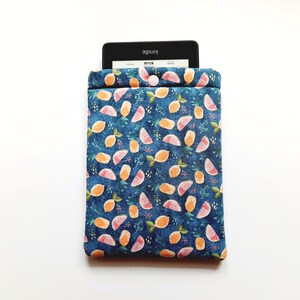 May include: A blue fabric Kindle sleeve with a pattern of orange lemons and pink watermelon slices. The sleeve has a button closure and a Kindle device is partially visible inside. The background is white.