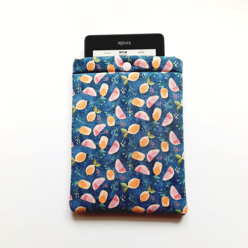 May include: A blue fabric Kindle sleeve with a pattern of orange lemons and pink watermelon slices. The sleeve has a button closure and a Kindle device is partially visible inside. The background is white.