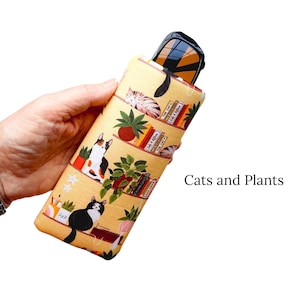 Pu&ograve; includere: Un astuccio giallo per occhiali con un motivo ripetuto di gatti, piante e libri. L'astuccio contiene un paio di occhiali da sole. Il testo "Cats and Plants" &egrave; visibile. L'astuccio &egrave; lungo circa 18 cm.