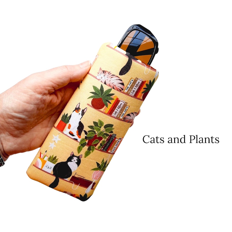 Pu&ograve; includere: Un astuccio giallo per occhiali con un motivo ripetuto di gatti, piante e libri. L'astuccio contiene un paio di occhiali da sole. Il testo "Cats and Plants" &egrave; visibile. L'astuccio &egrave; lungo circa 18 cm.