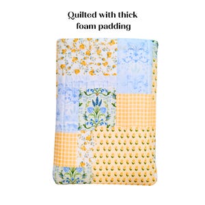 May include: A patchwork quilt with floral and gingham patterns in yellow, blue, and white. The quilt features a variety of designs, including floral prints and a gingham pattern. The text "Quilted with thick foam padding" is at the top.