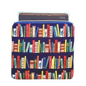 May include: A dark blue fabric sleeve featuring a repeating pattern of colorful vintage book spines with titles like Gulliver Travels, Heidi, and Treasure Island. A black Kobo e-reader is partially inserted into the top of the zippered pouch.