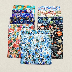 May include: A collection of rectangular fabric pouches featuring various floral and botanical patterns in vibrant colors. Each pouch is secured with a single plastic snap button in a contrasting color, arranged in two vertical stacks.