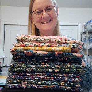 May include: A stack of colorful fabric with floral patterns. The fabric is folded and stacked neatly. The fabric is in various shades of blue, green, yellow, pink, and white.