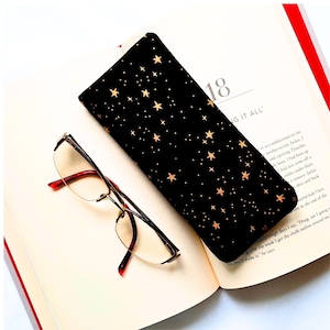 May include: Black glasses case with a gold star pattern. The case is lying open on a book with the text "NG IT ALL" visible.