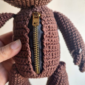 May include: A brown crocheted plush toy with a gold zipper down the back. The zipper has the word "OPTI" printed on it.