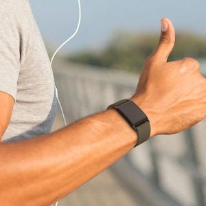 May include: A dark gray fitness tracker with a smooth, rectangular screen and a matching silicone band worn on the wrist. The device features a minimalist design with no visible buttons, showcasing a sleek, solid-colored strap and casing.
