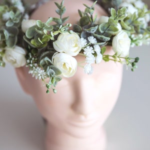 May include: A white flower crown with green leaves and small white flowers.