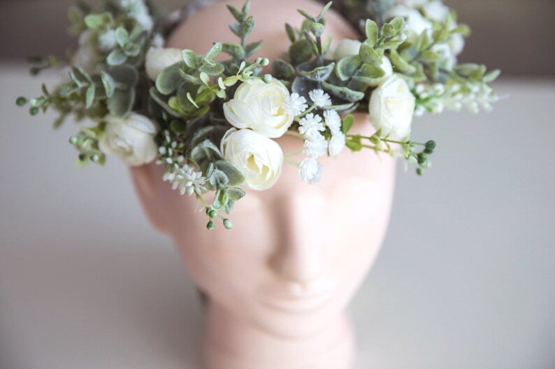 May include: A white flower crown with green leaves and small white flowers.
