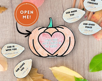 Puede incluir: Una manualidad con forma de calabaza con un centro en forma de corazón, con el texto "I WILL HIDE GOD'S TRUTH IN MY HEART". La imagen incluye recortes adicionales con versículos bíblicos y el texto "OPEN ME!" en una etiqueta circular. La manualidad está sobre una superficie de madera.