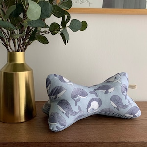 May include: A light blue pillow with a whale pattern. The pillow is shaped like a bone and has a soft, plush texture.