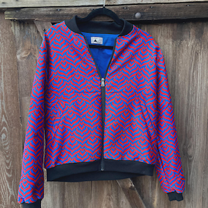 Könnte beinhalten: Eine langärmelige Bomberjacke mit einem sich wiederholenden rot-blauen blattartigen Muster. Die Jacke hat einen schwarzen gerippten Kragen, Bündchen und Saum, einen durchgehenden Frontreißverschluss und ein einfarbig blaues Innenfutter.