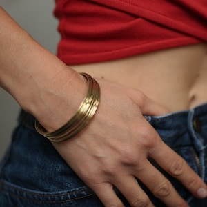 Pode incluir: Uma pessoa vestindo uma blusa vermelha e jeans azul com uma pulseira de ouro no pulso.